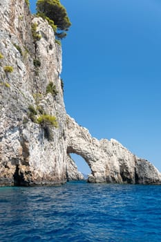 Beautiful view of a natural rocky small arch in the blue sea on a sunny summer day with clear skies on zakynthos island, side view close up.