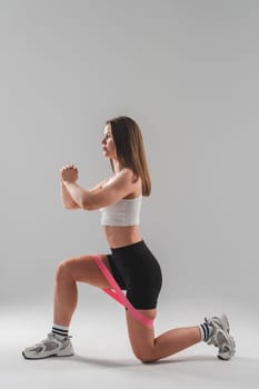 Caucasian woman doing exercises with a fitness elastic band on a white background. Vertical photo