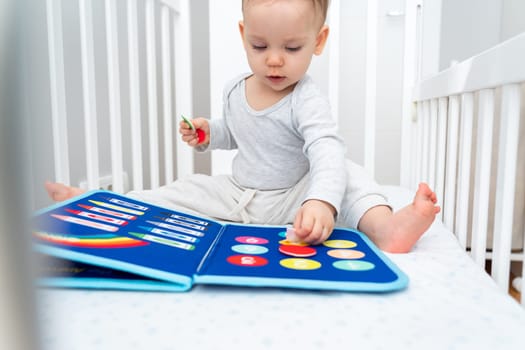 One year old baby playing with montessori busy book sitting in crib. ducational books and quiet books concept. Montessori busy board
