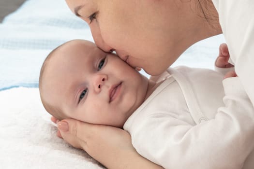 Mother is kissing her baby s nose on a bed.