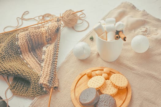 Hot drink with marshmallows and a tube of cinnamon. cookies with Christmas needles. unfinished scarf with knitting needles