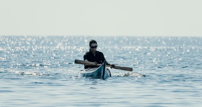 Happy smiling woman in kayak on ocean, paddling with wooden oar. Calm sea water and horizon in background