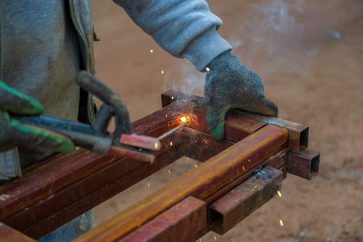 Welder welding two iron profiles at the construction site on a sunny day