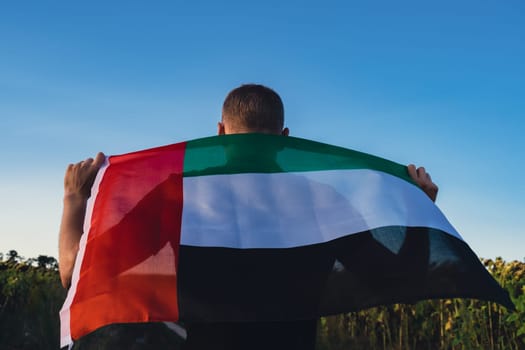 Man showing National Flag Of UAE Waving In The Wind during sunset. National Independence Day or Flag day. Flag of United Arab Emirates on Sun Background. Sign of Dubai.