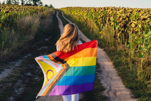 Equal rights to all. Young woman holding Rainbow LGBTQIA flag waving in wind made from silk material on field background. Symbol of LGBTQ pride month. Peace and freedom concept