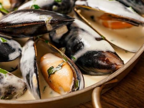 Delicious black mussels in creamy cheese and garlic sauce. Mediterranean black mussels in metal pan on wooden cutting board with grilled bread on wooden background