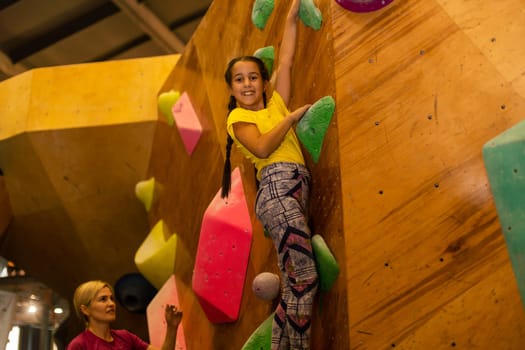 little girl climbing a rock wall indoor.