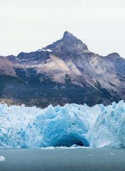 A glacier with a blue facade and a vast ice cave, nestled among rugged mountains.