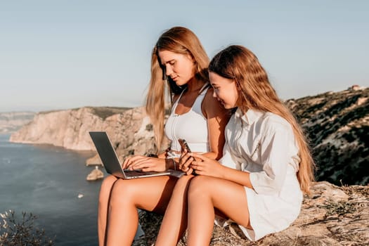 Successful business woman in yellow hat working on laptop by the sea. Pretty lady typing on computer at summer day outdoors. Freelance, travel and holidays concept.