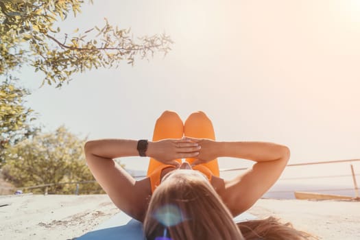 Fitness woman sea. Outdoor workout on yoga mat in park near to ocean beach. Female fitness pilates yoga routine concept. Healthy lifestyle. Happy fit woman exercising with rubber band in park.