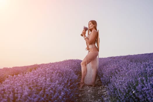 Close up portrait of young beautiful woman in a white dress and a hat is walking in the lavender field and smelling lavender bouquet.