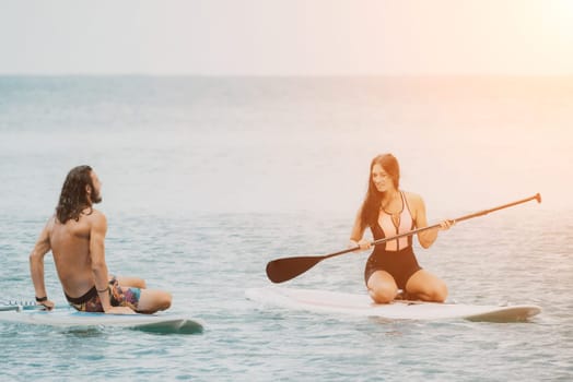 Sea woman and man on sup. Silhouette of happy young woman and man, surfing on SUP board, confident paddling through water surface. Idyllic sunset. Active lifestyle at sea or river