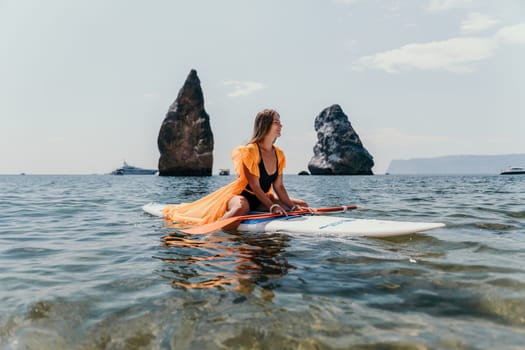 Close up shot of beautiful young caucasian woman with black hair and freckles looking at camera and smiling. Cute woman portrait in a pink bikini posing on a volcanic rock high above the sea