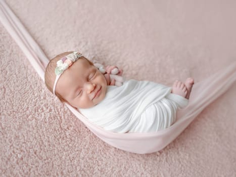Newborn Baby, Swaddled In A Blanket, Sleeps In A Hammock During A Photo Session With A Smile