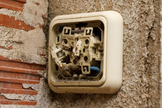 Detail view of a broken electrical switch mounted on a brick wall.