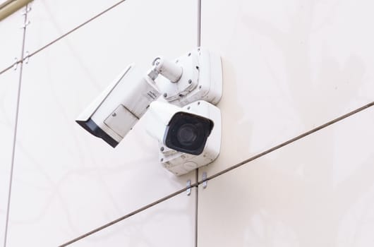 Two security cameras positioned back-to-back for surveillance mounted on a clean white exterior wall of a building.