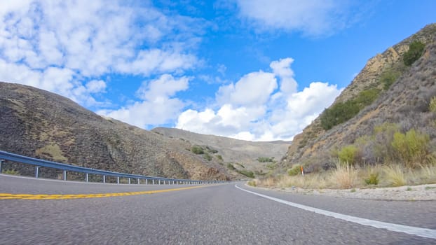 Vehicle is cruising along the Cuyama Highway under the bright sun. The surrounding landscape is illuminated by the radiant sunshine, creating a picturesque and inviting scene as the car travels through this captivating area.