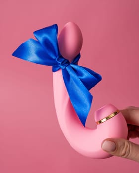 Woman holding curved dildo with blue ribbon on pink background