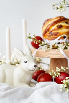 Festive table setting with ceramic bunny, red eggs, candles and Easter pastries. Easter holiday concept