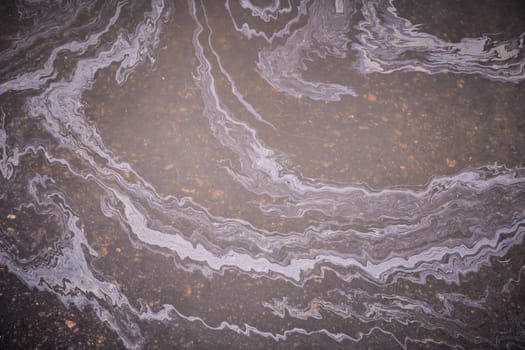Marble spills on the water from stains of gasoline and oil. Abstract background from motor oil, gas or petrol spilled on asphalt.