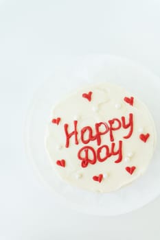 A white cake with Happy Day written in red icing, surrounded by small red hearts and white pearls