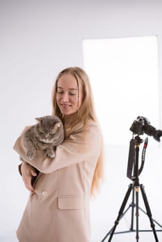 A business woman, freelancer, blogger in suit is working on a white floor, black background. blonde assistant in video production with camera and scottish straight cat