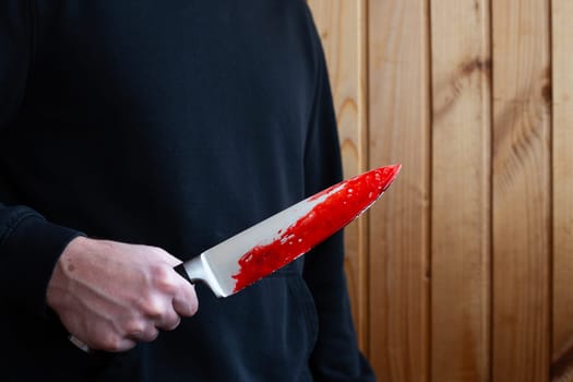 Killer holds bloody knife in his hand, bloody weapon is murder after crime in hands of maniac