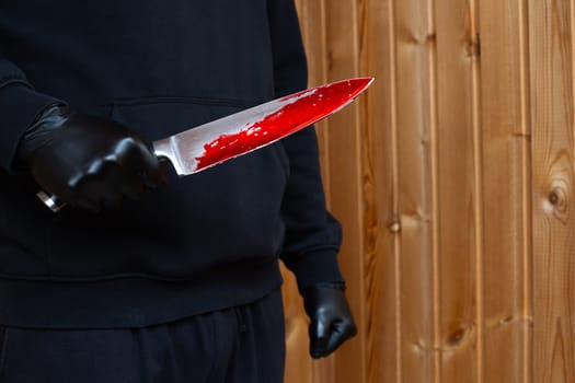 Maniac holds bloody murder weapon in his hand, killer in black gloves holding knife with dripping blood