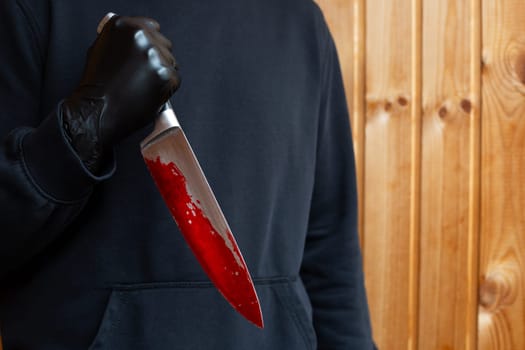 Maniac holds bloody knife with reverse grip, bloody sharp murder weapon in hands of killer in black clothes