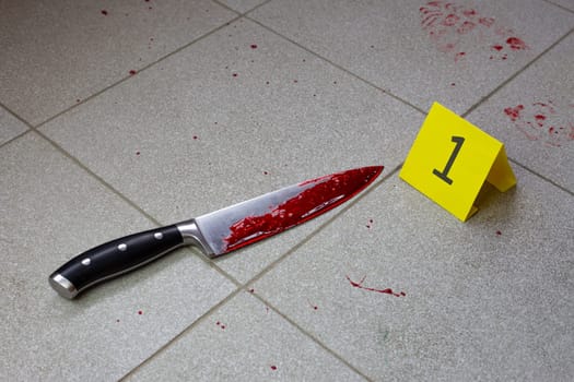Bloody knife at crime scene next to evidence number, evidence timeline identifier on tile floor