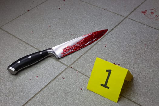 Knife covered in blood on the floor near the evidence identification sign at the crime scene