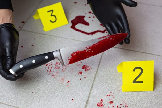 Criminologist holds in his hands in black gloves murder weapon at crime scene, bloody knife in the hands of policeman