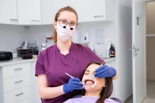 Dentist in glasses doing an examination of teeth for patient in dental office.