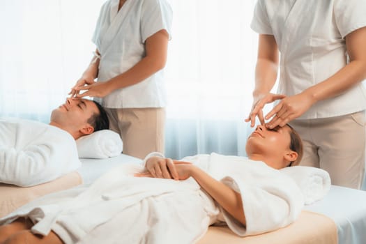 Caucasian couple enjoying relaxing anti-stress head massage and pampering facial beauty skin recreation leisure in dayspa modern light ambient at luxury resort or hotel spa salon. Quiescent