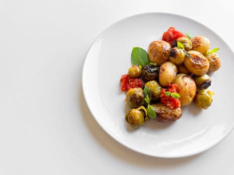 Roasted baby potatoes and Brussels sprouts with cherry tomatoes on white plate, garnished with basil, healthy vegetarian dish concept with space for text. High quality photo