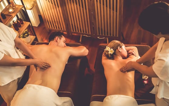 Caucasian couple customer enjoying relaxing anti-stress spa massage and pampering with beauty skin recreation leisure in warm candle lighting ambient salon spa at luxury resort or hotel. Quiescent