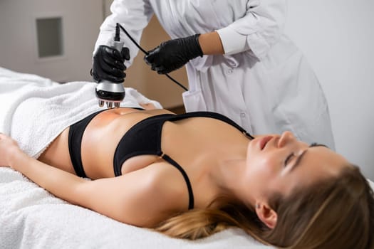 Young woman is lying while getting RF lifting of the body in a spa beauty salon