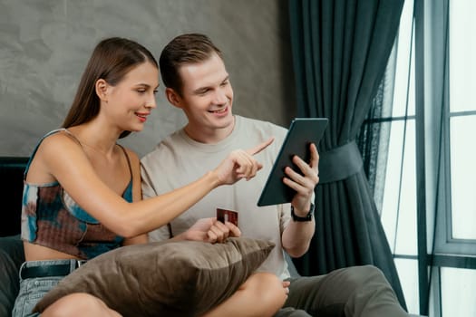 Young couple sit in the home bedroom using online payment app and digital wallet on smartphone to pay with credit card. E commerce shopping and modern purchasing via mobile internet. Unveiling