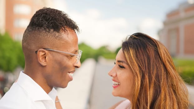 Multiethnic couple outdoors, looking at each other smiling.