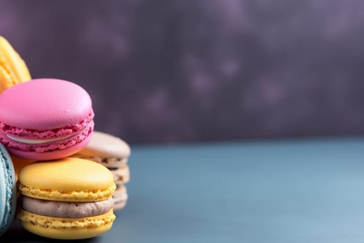 Assorted colorful macarons stacked against a purple backdrop.