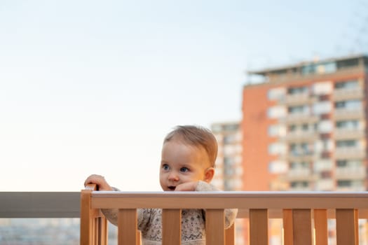 smiling baby looks out of the crib against the backdrop of a city landscape.