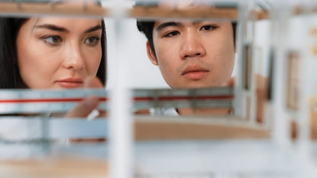 Close up of cooperative professional engineer working together to measuring house model structure. Young beautiful architect measure house model while male engineer support performance. Immaculate.