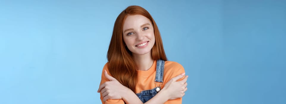 Lifestyle. Tender silly redhead girl standing blue background smiling joyfully hugging arms crossed body feel chilly grinning delighted talking boyfriend romantic date asking lend jacket cold summer evening.