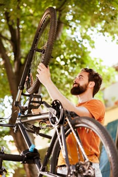 Focused young male cyclist ensures bike is well-prepared for outdoor adventures by diligently securing tire rubber. Healthy and active man holding bicycle wheel for maintainance.