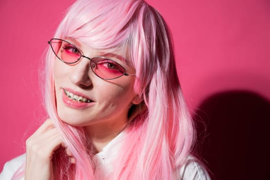 Close-up portrait of a young woman with braces in a pink wig and sunglasses on a pink background