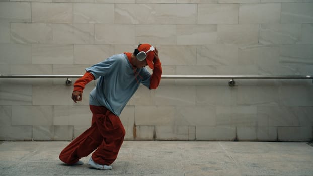 Handsome choreographer practice street dance in gray background. Young attractive b-boy dancer perform while wearing stylish cloth. Feeling of lively step. Copy space. Outdoor sport 2024. Sprightly.