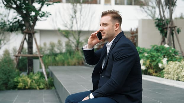 Side view of businessman sitting at park while talking to investors about marketing strategy. Caucasian executive manager looking increasing sales or successful project at eco city. Lifestyle. Urbane