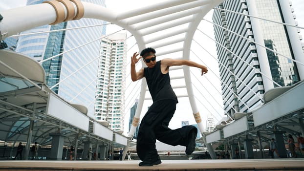 Young asian hipster show footstep at city center surround by people. Stylish fashion street dancer perform B-boy or freestyle dancing with low angle. Outdoor sport 2024. Break dancing. Sprightly.