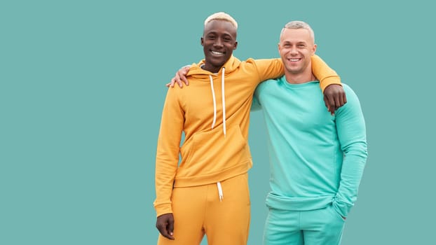 Multi ethnic friends. Two men different color black African-American ethnicity and white Caucasian ethnicity standing isolated green background. Dressed active sportswear. interracial friendship