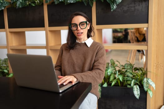 Woman Wearing Glasses using Laptop. Charming businesswoman in eyeglasses and casual clothes working with laptop computer looking at camera.